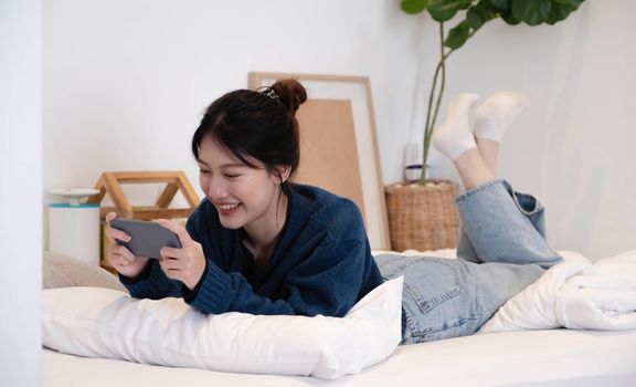 Portrait beautiful young asian woman on a white mattress in the bedroom in the morning.The smartphone is in the hands of women. Lady holding phone..