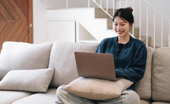 asian woman with laptop lying on comfy sofa and working remotely from home, mockup for website design.