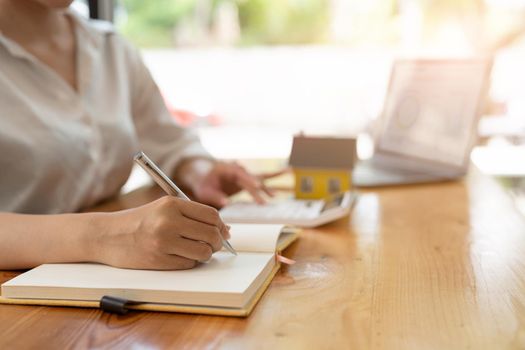 Close up real estate agent working with calculator taking note for financial loan on wooden desk.