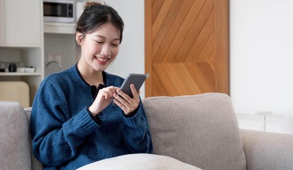 Portrait beautiful young asian woman use smart mobile phone on sofa in living room interior.