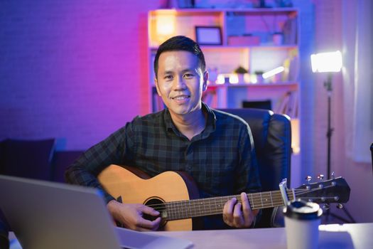 Asian man youtuber live streaming perfomance playing guitar and sing a song. Asian man teaching guitar and singing online. Musician recording music with laptop and playing acoustic guitar.