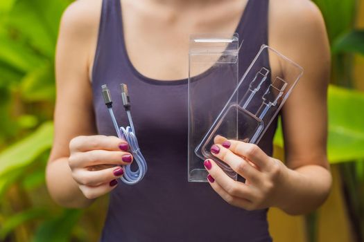 Female hands printed a new wire to charge the phone. The wire was packed in a large number of plastic packaging, which will be thrown into the trash. Zero waste concept. Plastic trash concept.