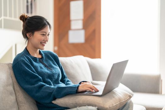 Smiling young woman using laptop, sitting on couch at home.