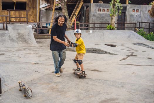 Athletic boy learns to skateboard with asian trainer in a skate park. Children education, sports. Race diversity.