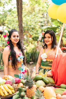 Vertical photo of two pretty Latin women in tropical dresses picking fruit during a harvest festival in Masaya Nicaragua