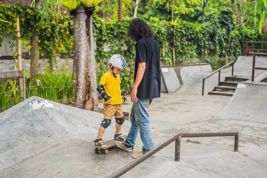 Athletic boy learns to skateboard with a trainer in a skate park. Children education, sports.