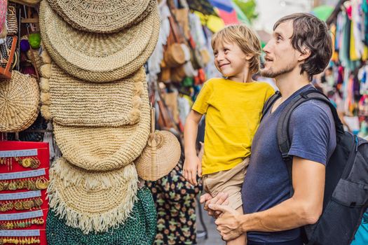 Dad and son at a market in Ubud, Bali. Typical souvenir shop selling souvenirs and handicrafts of Bali at the famous Ubud Market, Indonesia. Balinese market. Souvenirs of wood and crafts of local residents. Traveling with children concept. Kids friendly place.