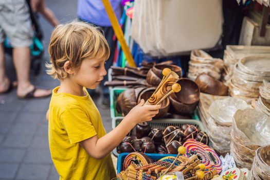 Boy at a market in Ubud, Bali. Typical souvenir shop selling souvenirs and handicrafts of Bali at the famous Ubud Market, Indonesia. Balinese market. Souvenirs of wood and crafts of local residents. Traveling with children concept. Kids friendly place.