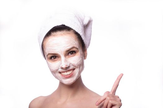 woman in a white towel on her head with a white cosmetic mask on her face, white background, close-up portrait. High quality photo
