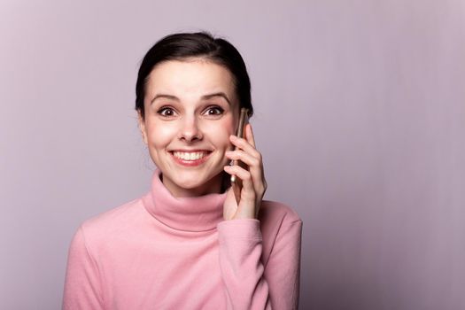 beautiful girl in a pink turtleneck talking on the phone on a gray background. High quality photo