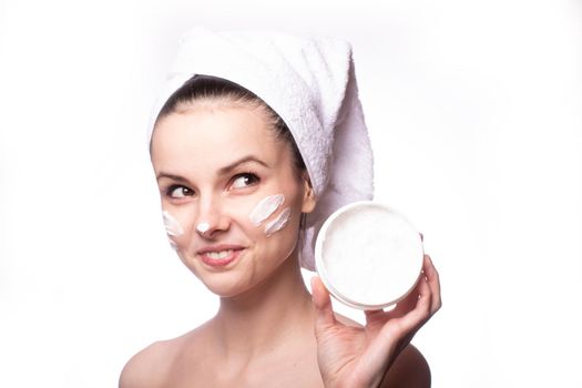 a woman with a white towel on her head and a cream on her face holds a package of cream in her hands. High quality photo