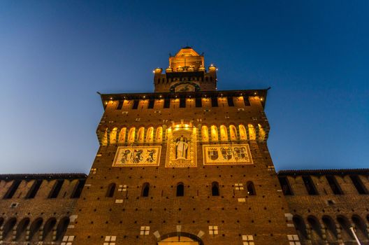 Old medieval Sforza Castle Castello Sforzesco lightning facade, walls, tower La torre del Filarete with lights at sunset, dusk, twilight, evening, blue sky, view below, Milan, Lombardy, Italy