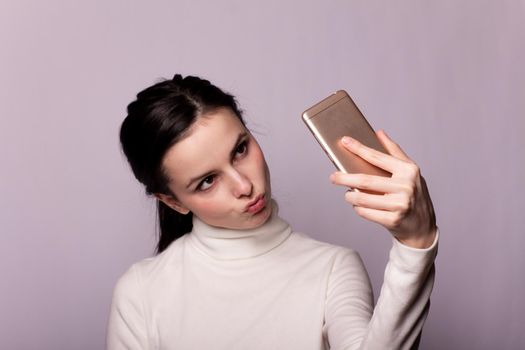 woman in a white turtleneck talking on the phone, portrait on a gray background. High quality photo