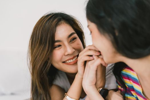 Beautiful asian young lesbian LGBTQ couple or friends using computer laptop together smile and relax on bed.Happiness LGBTQ couple woman spending time together at home. LGBTQ Pride Month Concept.