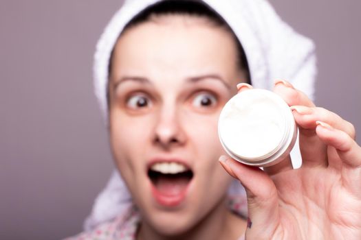 a brunette woman in a towel on her head holds a package of cosmetic cream in front of her. High quality photo