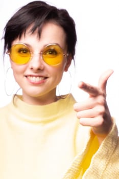 brunette woman in yellow glasses and yellow sweater, close-up portrait, white background. High quality photo