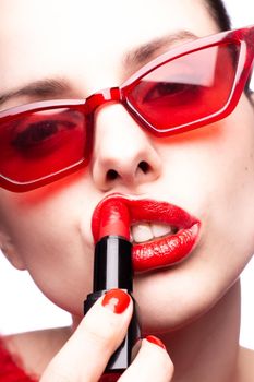 brunette woman in red sunglasses paints lips with red lipstick, red nails, white background. High quality photo
