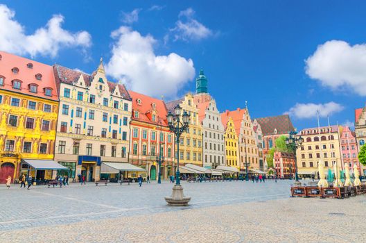 Row of colorful buildings with multicolored facade and St. Elizabeth Minor Basilica Garrison catholic Church on cobblestone Rynek Market Square in old town historical city centre of Wroclaw, Poland