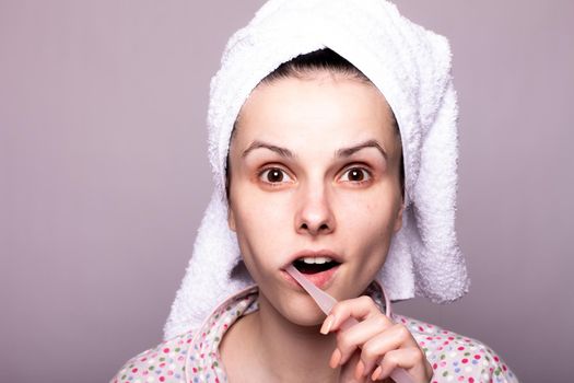 a woman in a towel on her head brushes her teeth, gray background, close-up. High quality photo