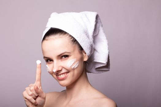 woman in a white towel on her head with cream on her face, gray background. High quality photo