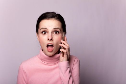 beautiful girl in a pink turtleneck talking on the phone on a gray background. High quality photo