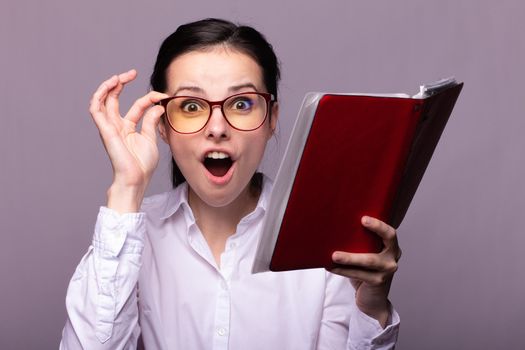 woman in a white shirt and glasses holds a red notebook in her hand. High quality photo