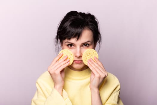cute brunette woman in a yellow sweater holds a cosmetic sponge in her hands. High quality photo