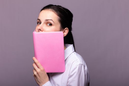 woman in a white shirt holds a pink notebook in her hands. High quality photo