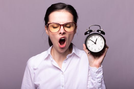 woman manager in a white shirt and glasses holds an alarm clock in her hand, gray studio background. High quality photo