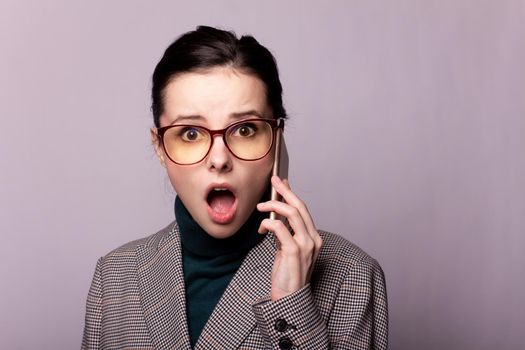 woman in a green turtleneck, jacket, glasses talking on the phone portrait on a gray background. High quality photo