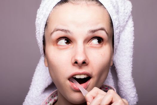 a woman in a towel on her head brushes her teeth, gray background, close-up. High quality photo