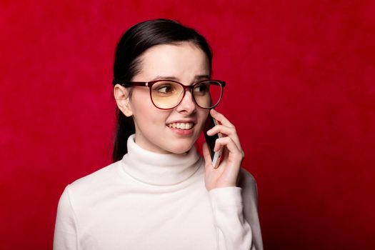 woman in a white turtleneck talking on the phone, portrait on a red background. High quality photo