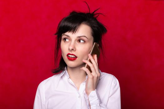 beautiful woman manager in a white shirt speaks on the phone, red lips, red background. High quality photo