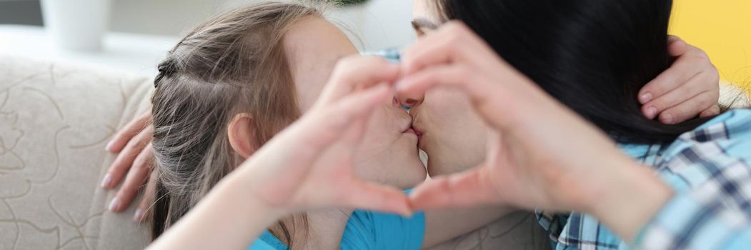 Mom gently kisses her little daughter, together they show a heart gesture, close-up. Love of parents and children, family relationships
