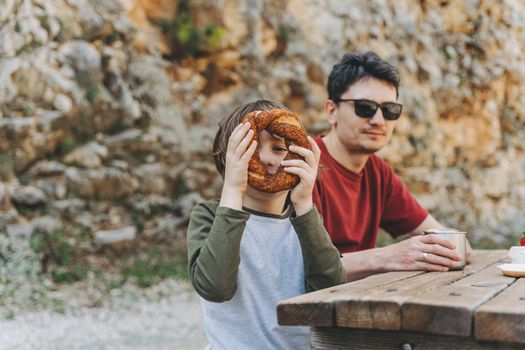 School boy kid child happily looking through donut bread while having a family picnic in the mountains with his father dad.