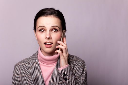 woman in a pink turtleneck, gray jacket, for sight communicates on the phone on a gray background. High quality photo
