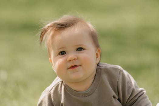 A close portrait of a 7-month child who is playing in the meadow. An infant girl is crawling on the grass.