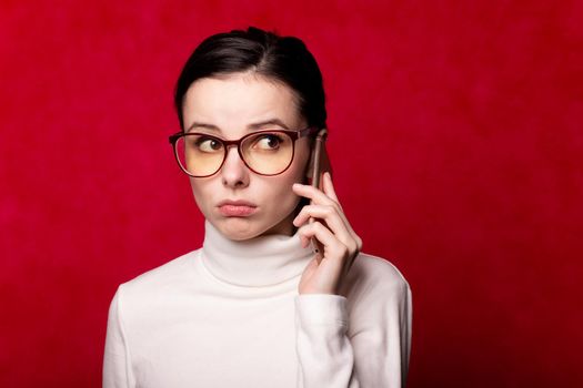 woman in a white turtleneck talking on the phone, portrait on a red background. High quality photo