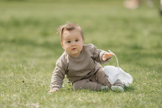 A smiling 7-month child is posing with a white panama hat in the meadow. An infant girl is crawling on the grass.