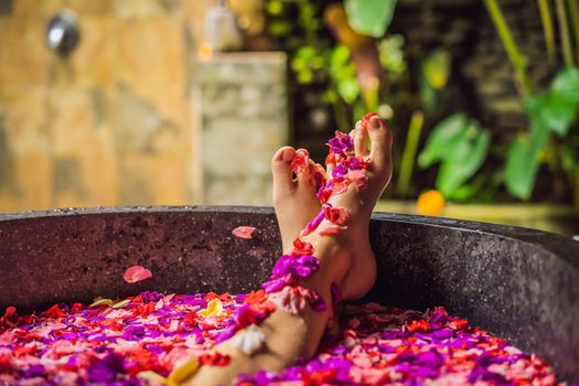 Attractive Young woman in bath with petals of tropical flowers and aroma oils. Spa treatments for skin rejuvenation. Alluring woman in Spa salon. Girl relaxing in bathtub with flower petals. Luxury.