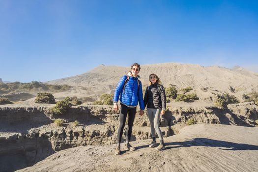 Young couple man and woman visit the Bromo volcano at the Tengger Semeru National Park on the Java Island, Indonesia. They enjoy magnificent view on the Bromo or Gunung Bromo on Indonesian, Semeru and other volcanoes located inside of the Sea of Sand within the Tengger Caldera. One of the most famous volcanic objects in the world. Travel to Indonesia concept.