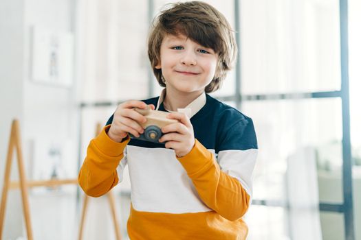 Smiling caucasian little Cute preschooler child boy having fun and playing with toy camera. Kid acting like a professional photographer taking photos at home in kids room. Background with copy space