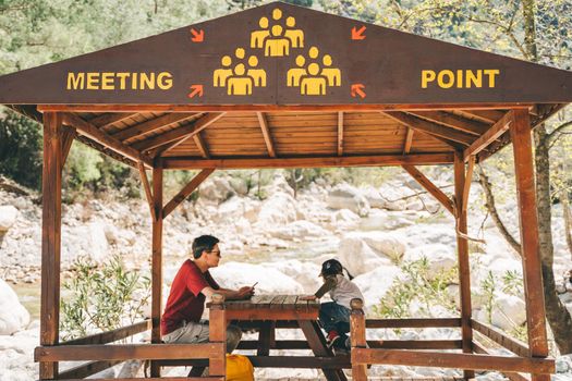 Dad and son sitting in community meeting point wooden hut in the mountains. School boy child and father taking rest in safety equipment construction - assembly gathering location station.