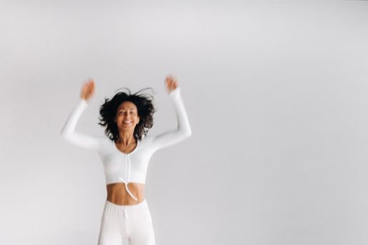 A blurry silhouette of a woman in white sportswear bounces on a white background. The girl, jumping, raised her hands up in the gym.