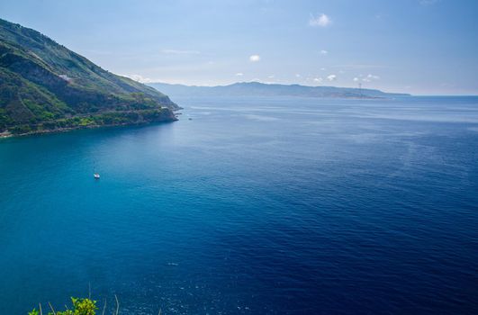 Aerial top view of green hill and harbour of beautiful seaside town village Scilla, Tyrrhenian sea bay gulf coast shore, Sicilia island and blue sky background, Calabria, Southern Italy