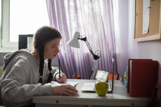 A student sits at her desk and studies using the internet and a personal computer. A diligent student. Remote learning at home.
