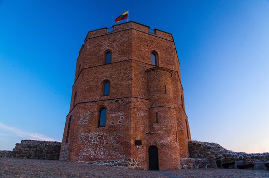 Medieval old Castle Tower Of Gediminas (Gedimino) on hill with Lithuanian national flag above at sunset, Vilnius, Lithuania