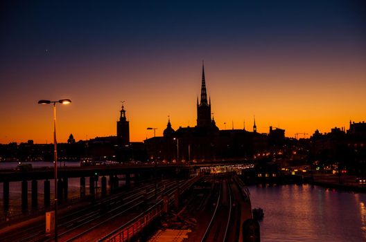 Silhouette of Stockholm cityscape skyline with Riddarholmen Church spires, City Hall Stadshuset tower, bridge over Lake Malaren in Gamla Stan at sunset, dusk, twilight and purple orange sky, Sweden