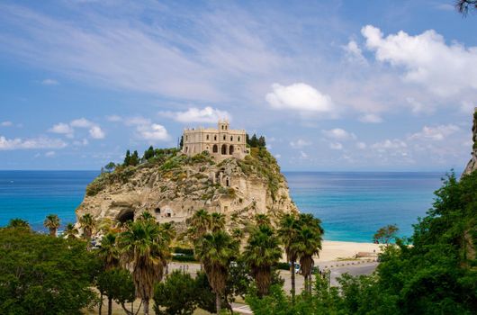 Monastery Sanctuary church Santa Maria dell Isola on top of rock of Tyrrhenian Sea and green palm trees, blue sky with white clouds around in sunny day, Tropea, Vibo Valentia, Calabria, Southern Italy