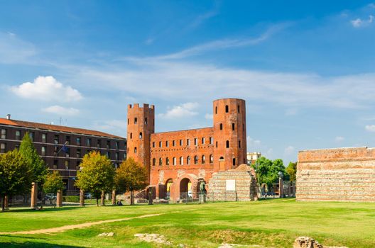 Palatine Gate Porta Palatina towers brick buildings is a Roman Age city ancient gate ruins with Julius Caesar statue and green lawn in historical centre of Turin Torino city, Piedmont, Italy